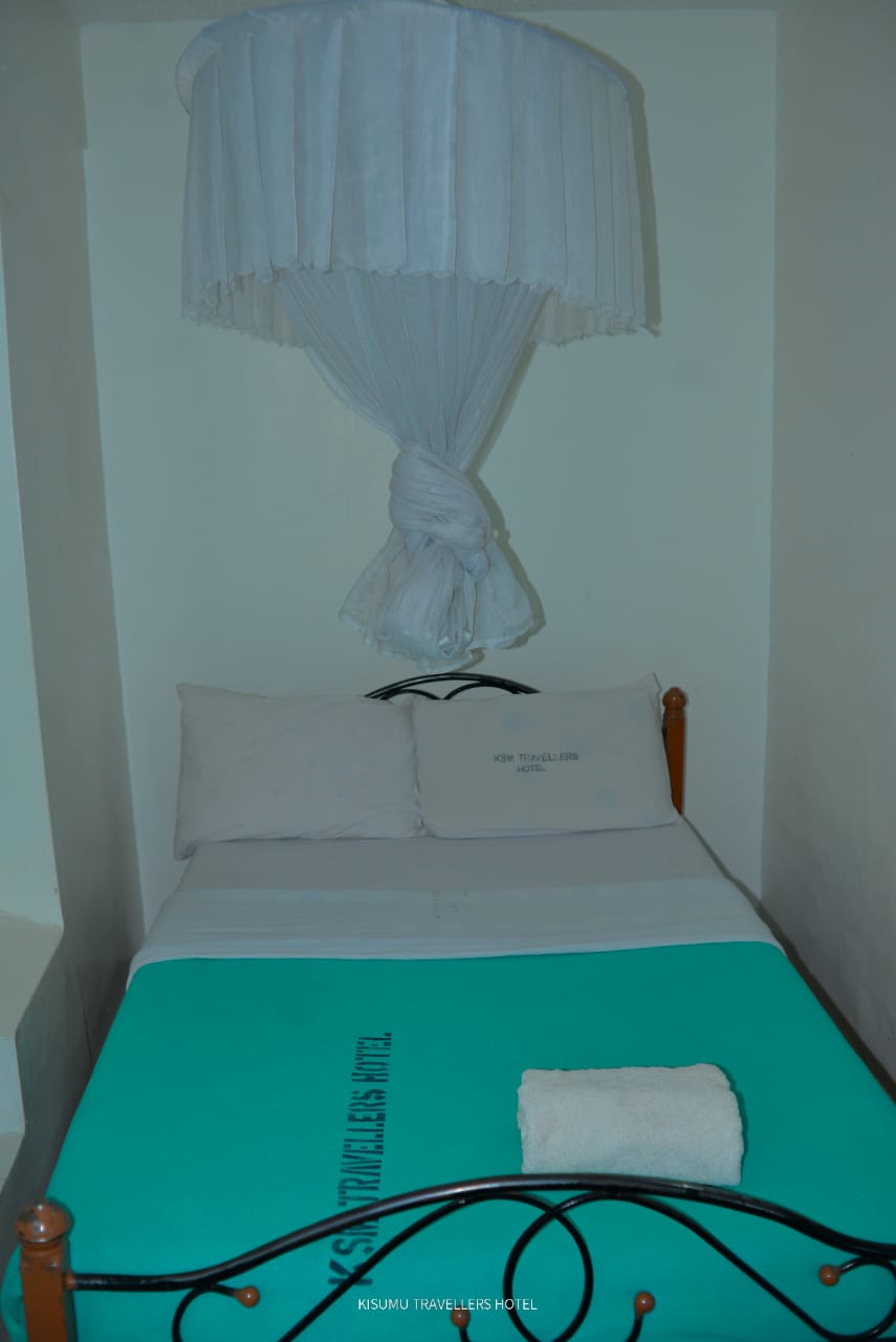 Non-self contained room with metal bed frame, turquoise bedding and mosquito net